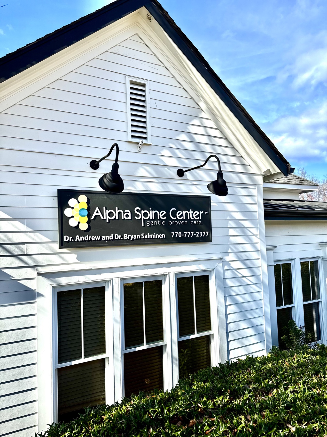 Alpha Spine Center’s white office building under a blue sky, with the sign for Dr. Andrew and Dr. Bryan Salminen