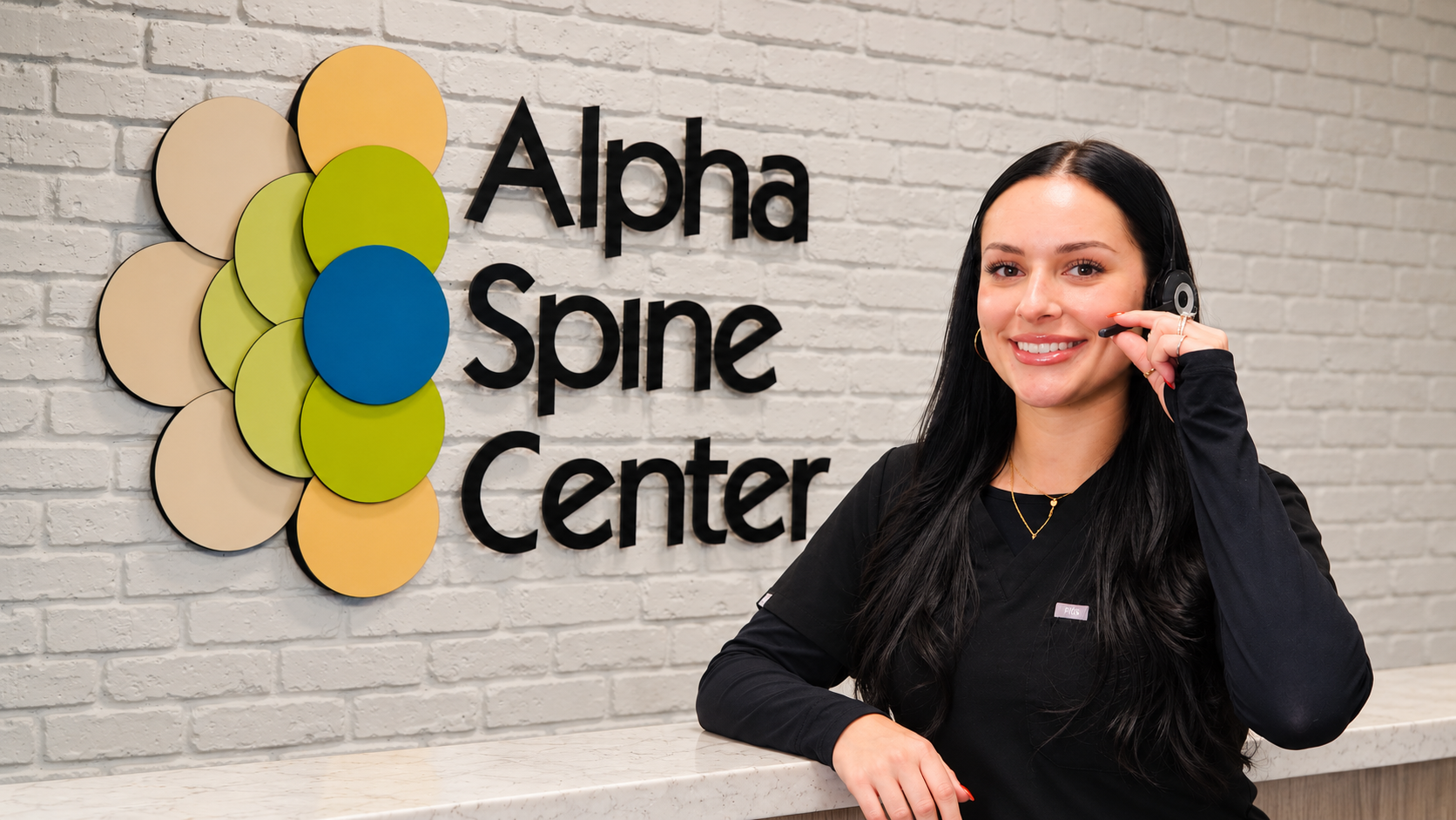 Stephanie smiling with her headset beside the Alpha Spine Center wall sign